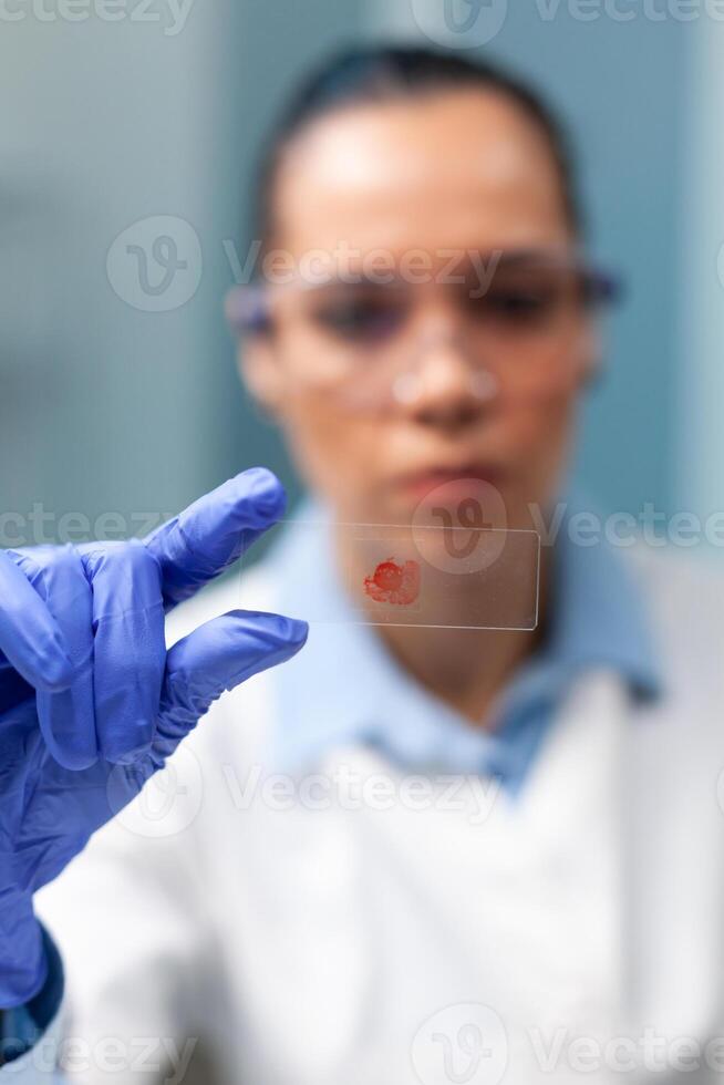 Chemist researcher holding glass with blood sample working at microbiology experiment in biochemistry hospital laboratory. Scientist woman doctor developing healthcare treatment against virus disease photo