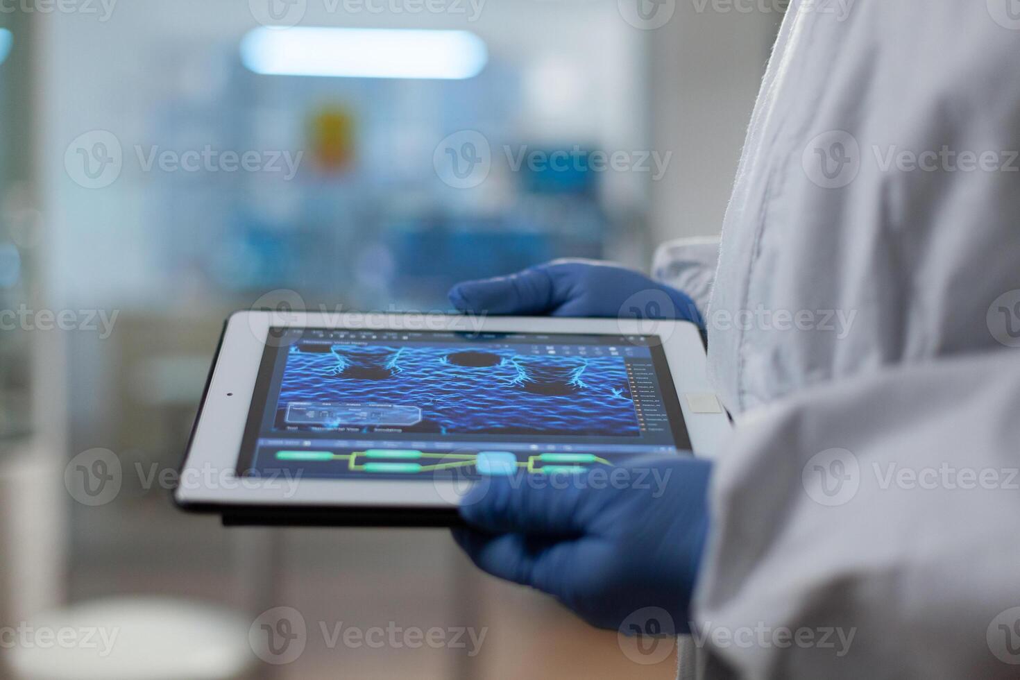 Scientist doctor wearing medical gloves and ppe suit holding tablet in hands analyzing virus development expertise working in biological hospital laboratory. Treatment investigation against covid19 photo