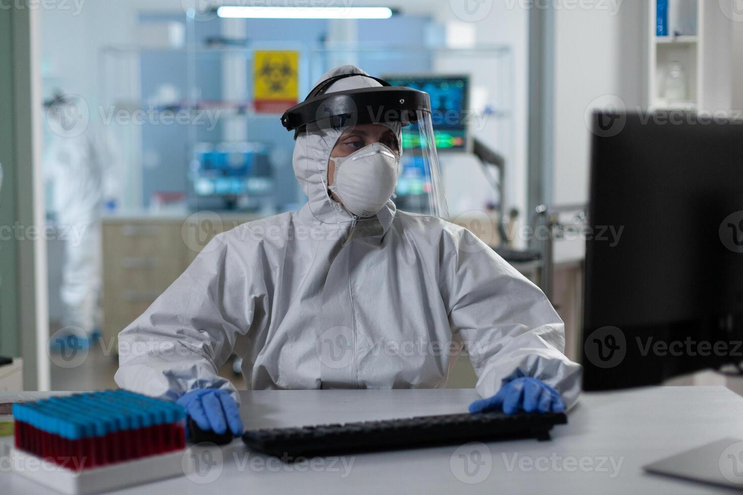 Scientist woman with protection medical equipment against covid19 typing covid19 test results working at vaccine development in scientific hospital laboratory. Virus prevention experiment photo