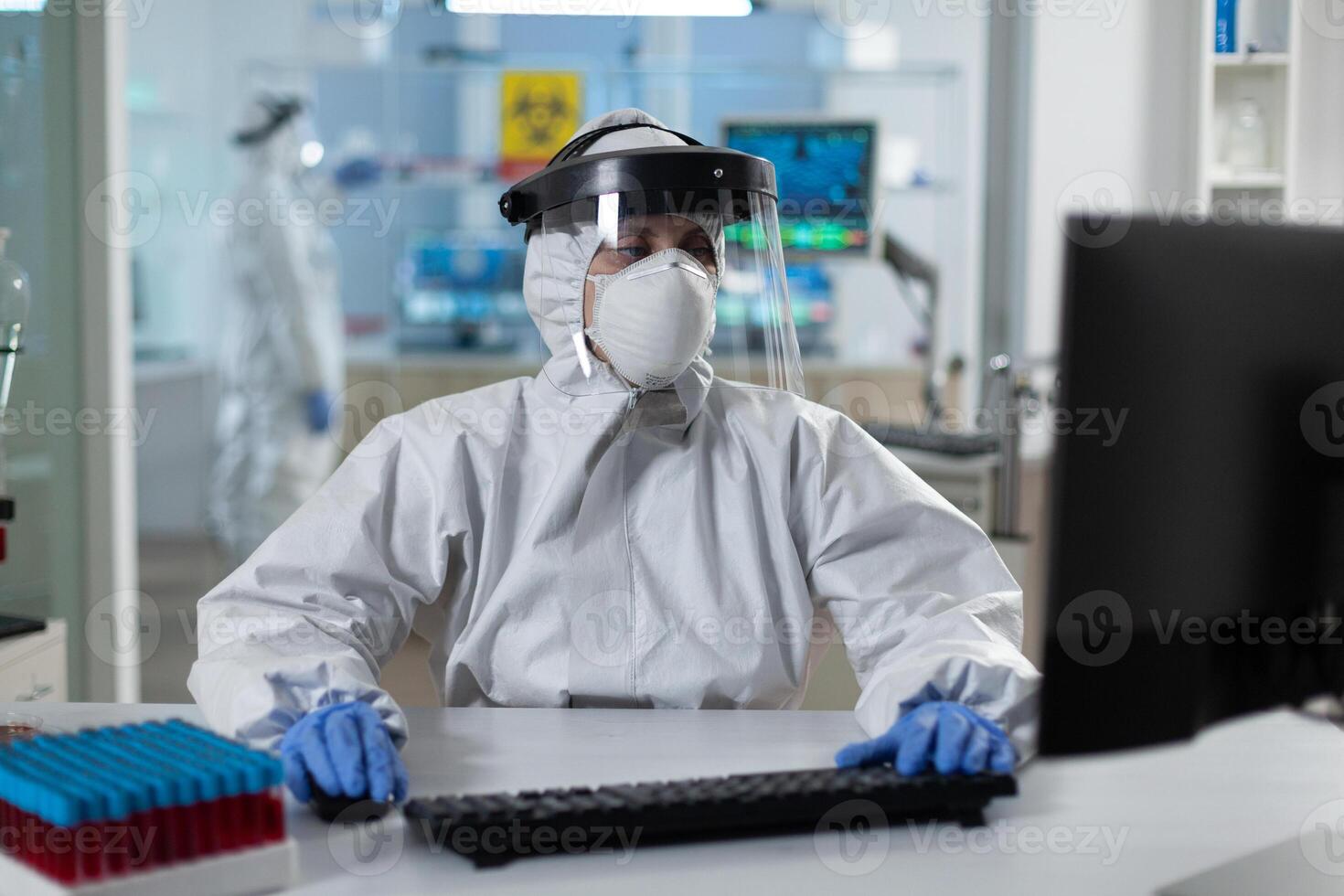 Scientist woman with protection medical equipment against covid19 typing covid19 test results working at vaccine development in scientific hospital laboratory. Virus prevention experiment photo