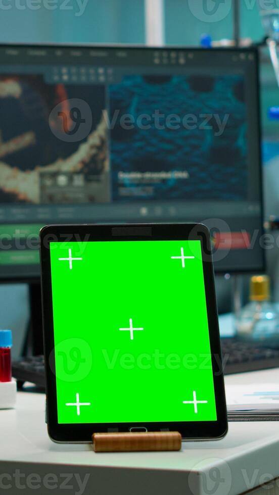 Scientist standing at monitor in background analysing virus evolution while tablet with mock-up green screen working in front. Man lab researcher examining vaccine developent bringing blood samples photo