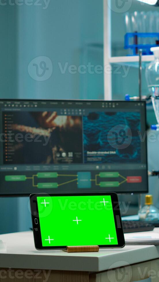 Tablet with green screen working in labooratory with mock up, chroma key display while professional engineer testing virus evolution in background. High tech development lab with blood samples photo