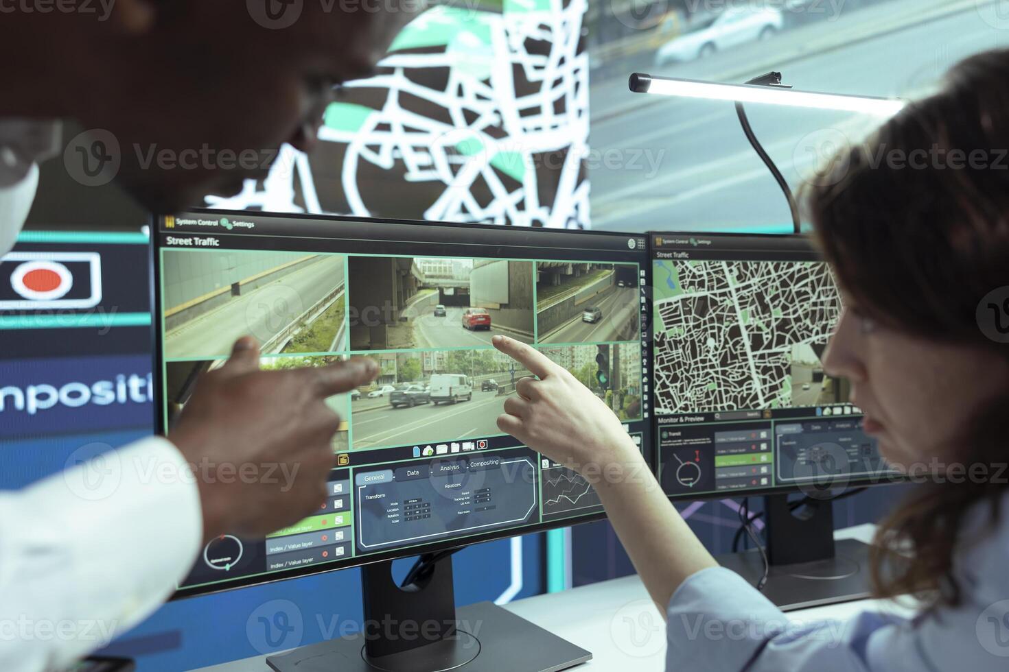 African american manager shows directions to a new employee, instructing her in how to use satellite map and CCTV system footage. People operating on government radar cameras to follow couriers. photo