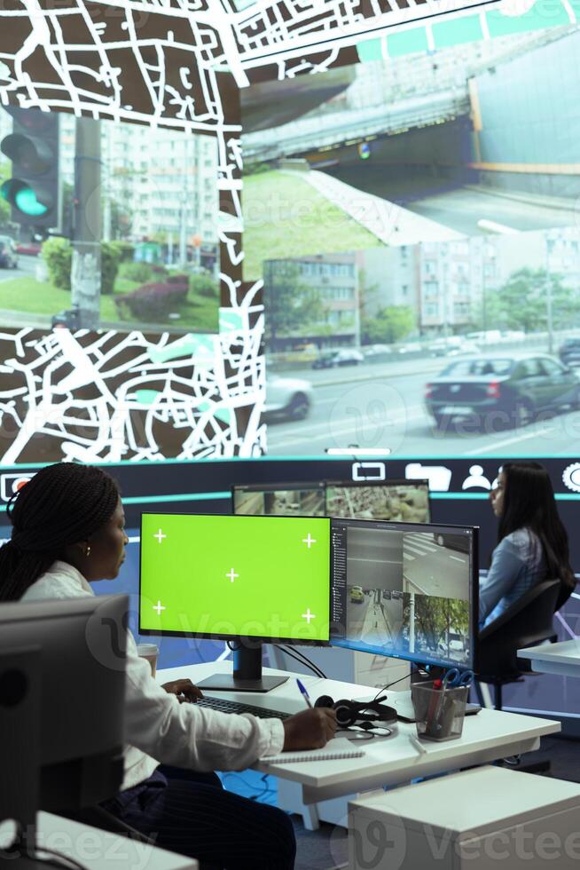 African american woman operator monitoring couriers in traffic via CCTV footage, using an isolated screen in control center. Dispatch employee uses gps coordinates to track cars. photo