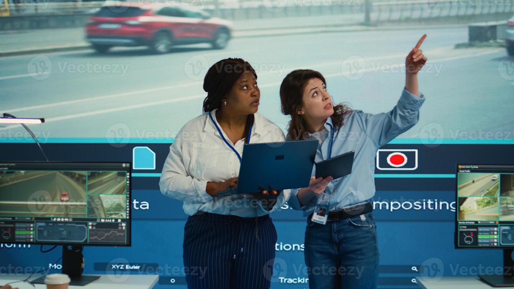 Diverse employees monitor and manage urban traffic in control center agency, following cars and their data through surveillance footage and CCTV networks. Government satellite sensors. Camera B. photo
