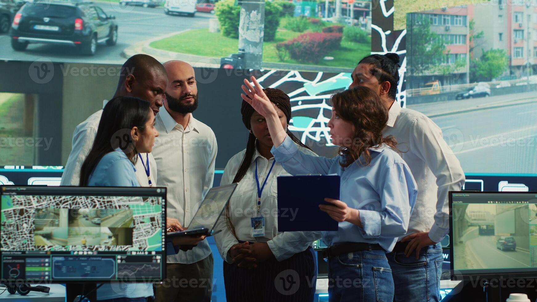 Diverse employees group discussing ways to speed up order delivery, looking for routes to avoid traffic on satellite navigation. Agency operators use CCTV footage in monitoring room. Camera A. photo