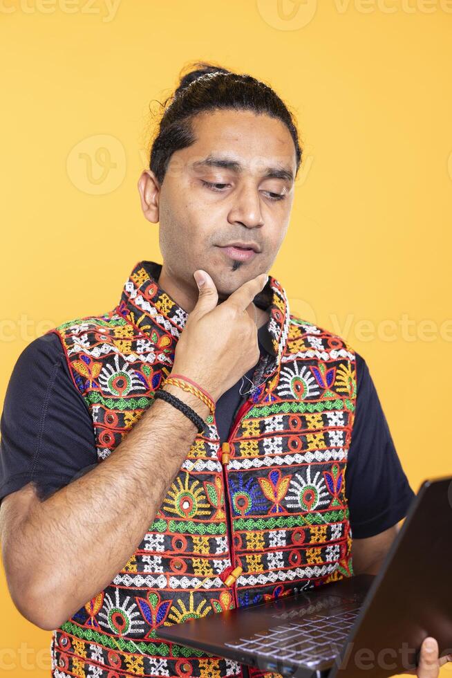 Pensive man thinking how to solve business tasks on laptop, isolated over studio background. Employee caught in brainstorming process, doing marketing analysis on notebook photo