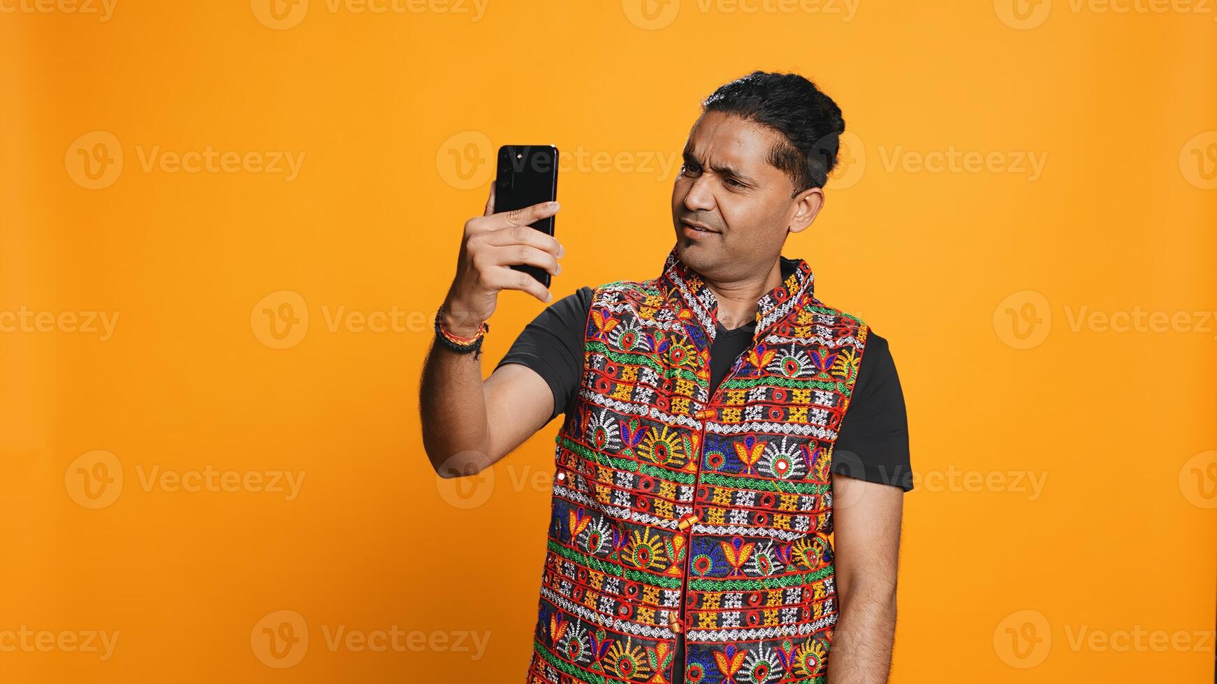 Happy man chatting with friend over online videocall on smartphone, doing friendly gestures. Smiling person communicating with mate on teleconference using mobile phone, studio background, camera B photo