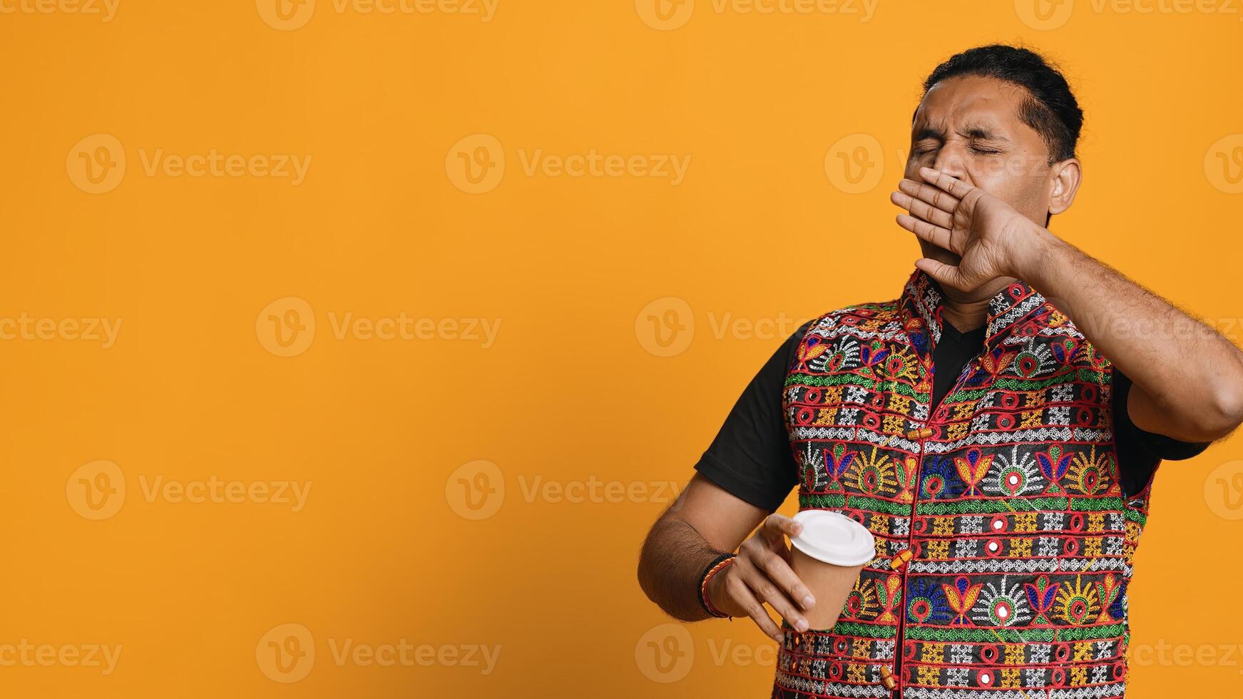 Sleepy man yawning and rubbing eyes. sipping coffee to wake up and gain energy. Exhausted person feeling fatigued after sleepless night, drinking caffeinated beverage, studio backdrop, camera A photo