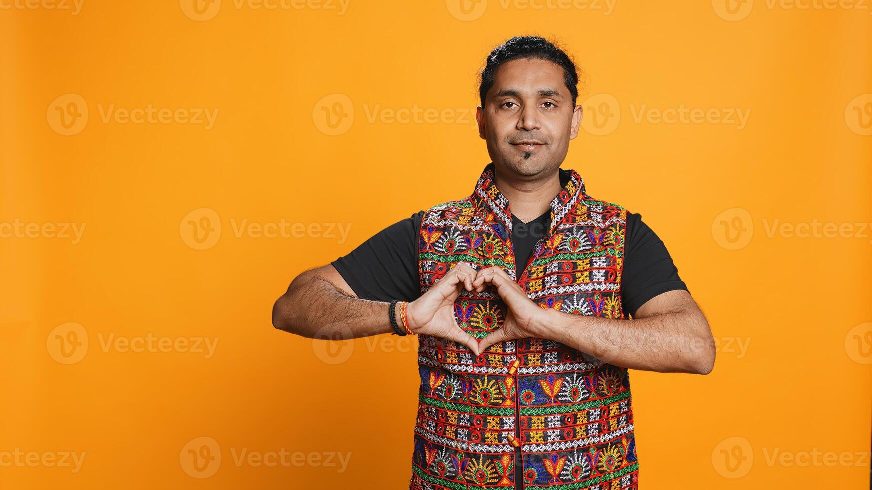 Portrait of smiling loving man doing heart symbol shape gesture with hands, showing kindness. Happy affectionate person doing tender love gesturing, isolated over studio background, camera B photo
