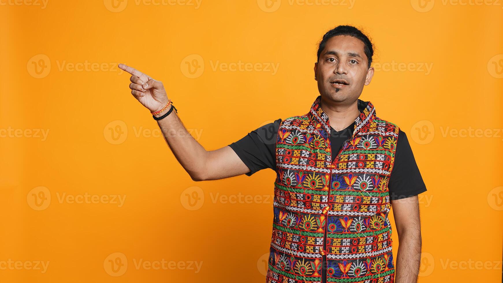 Salesman pointing around with finger, doing recommendation, talking with audience. Indian person showing copy text, doing advertisement, isolated over studio background, camera B photo