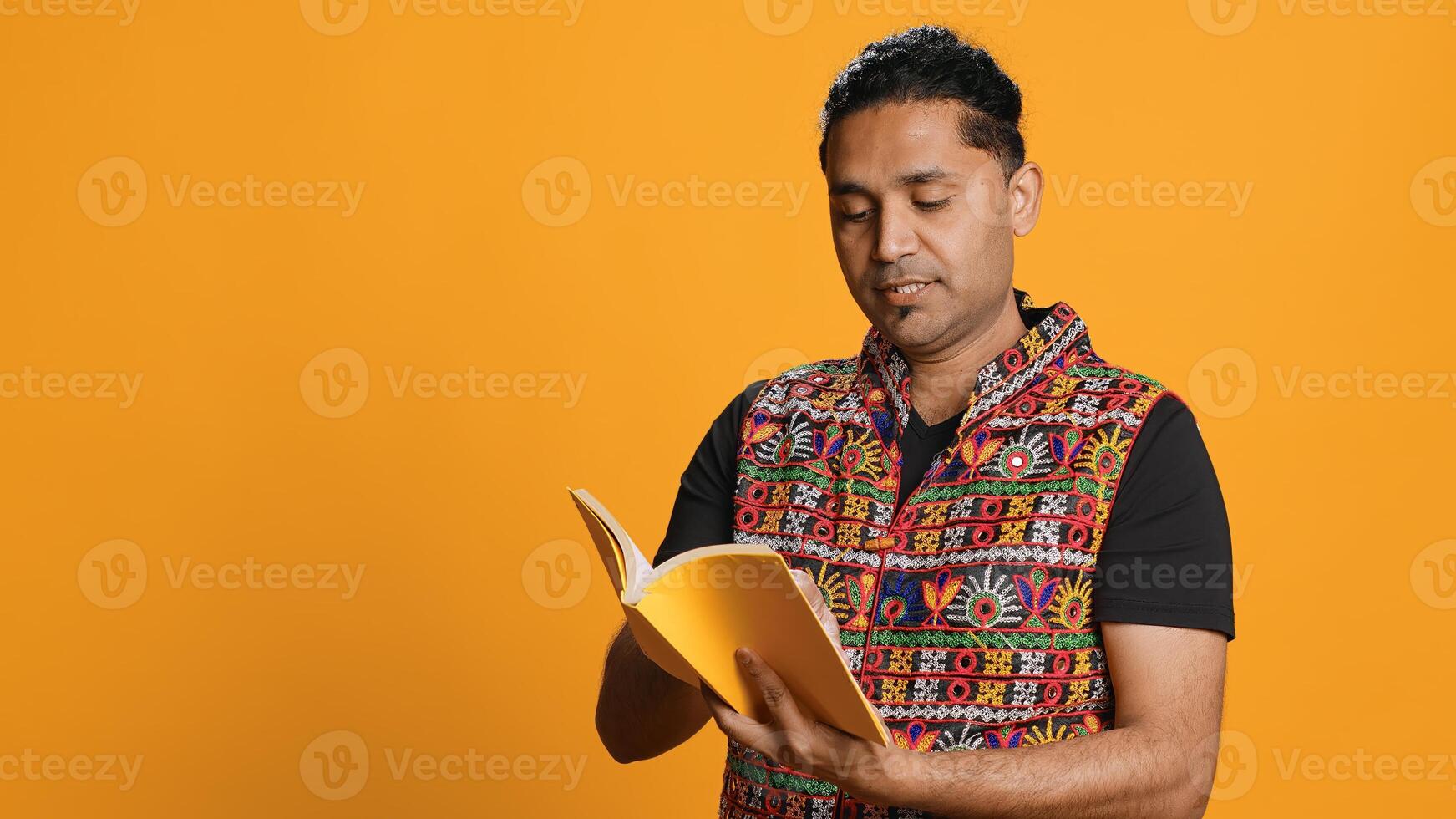 Indian man reading book, having fun and enjoying characters and plot, isolated over studio background. Relaxed person browsing novel, enjoying leisure time, appreciating literature, camera A photo