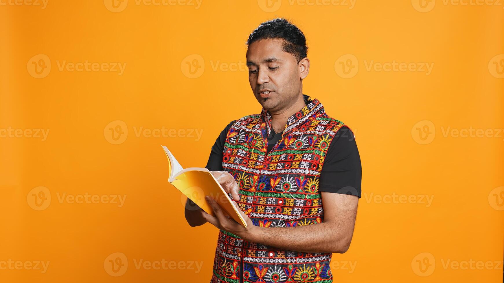 Indian man reading book, having fun and enjoying characters and plot, isolated over studio background. Relaxed person browsing novel, enjoying leisure time, appreciating literature, camera B photo