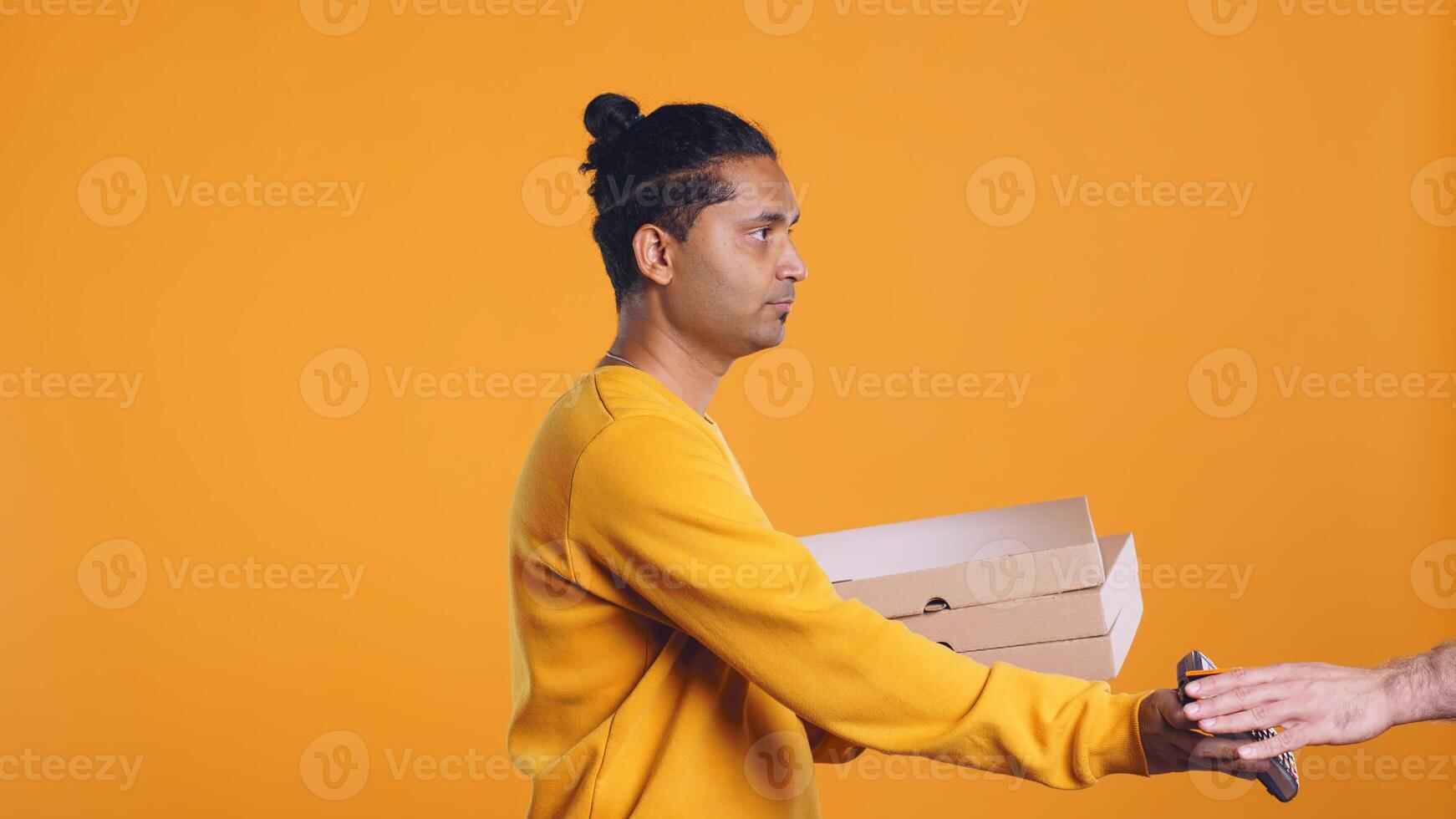 Portrait of indian pizza delivery man taking takeaway orders out of thermal backpack. Upbeat courier removing lunch boxes from transportation bag, isolated over studio background, camera B photo