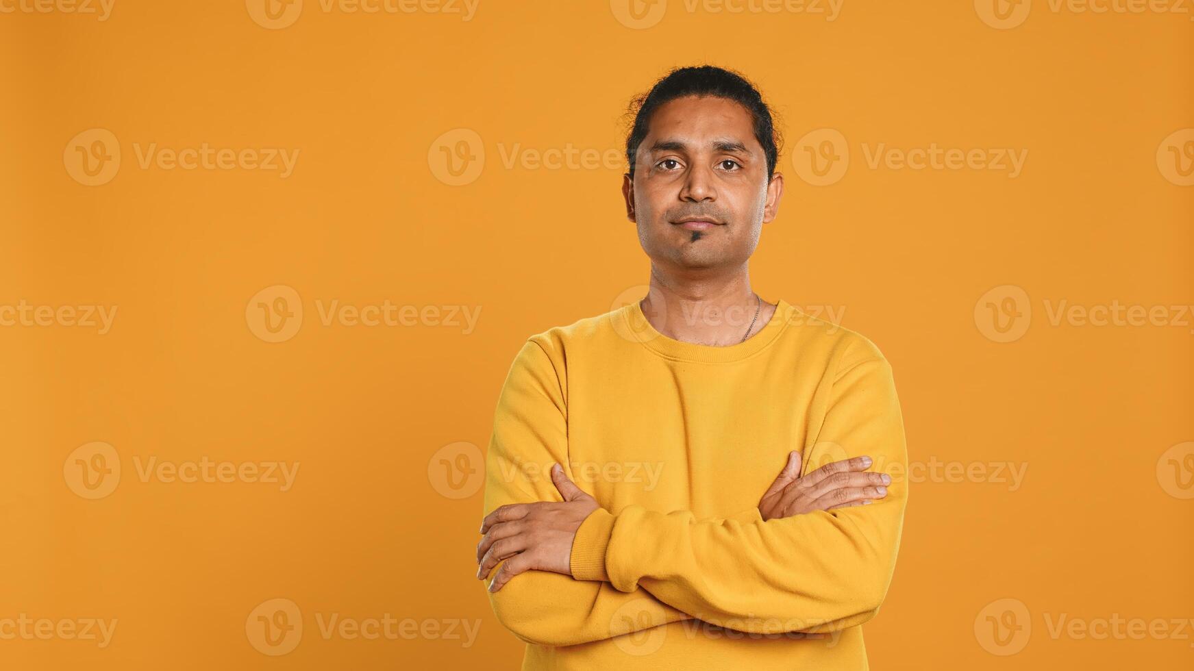 Portrait of cheerful friendly indian man smiling, looking pleased, isolated over yellow studio background. Happy expressive asian person grinning, feeling satisfied, camera A photo