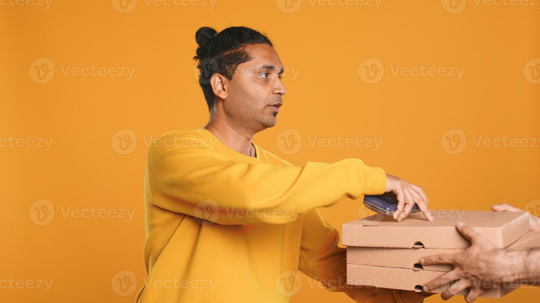 Pizza delivery man offering takeaway order to customer paying with credit card. Courier taking lunch boxes out of food backpack, giving POS to client to make transaction, studio background, camera A photo