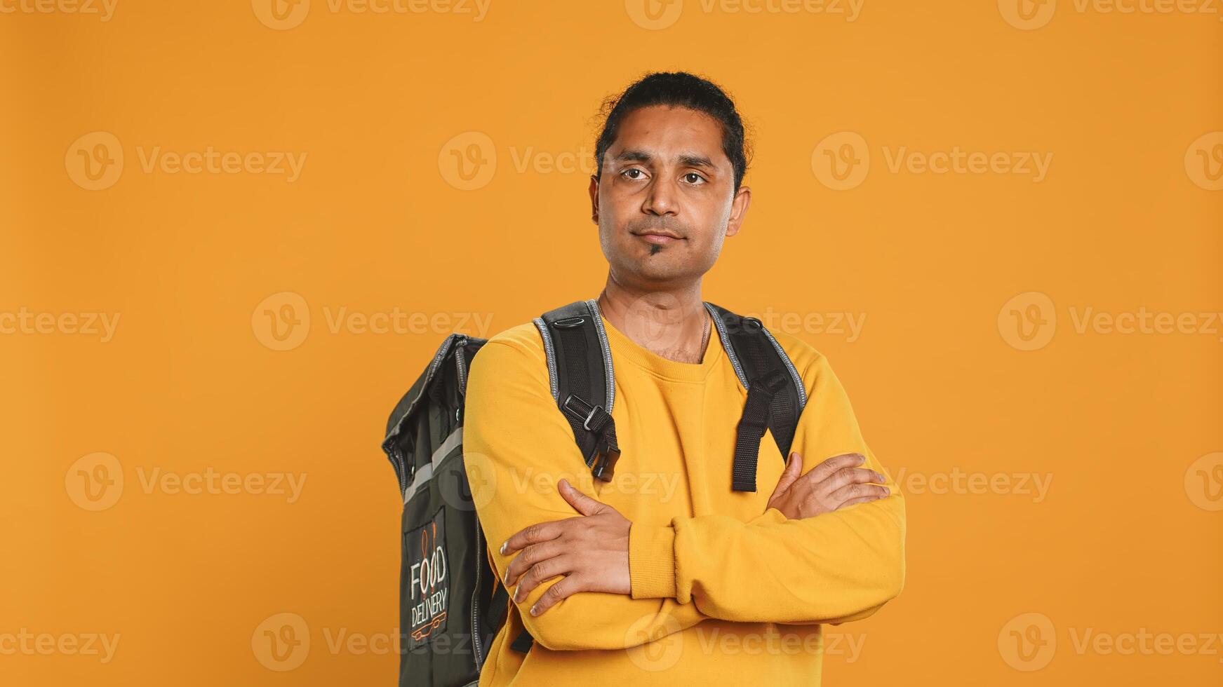 Portrait of upbeat indian man holding thermal backpack, isolated over studio background. Friendly cheerful person prepared to deliver takeaway food to customers, camera A photo