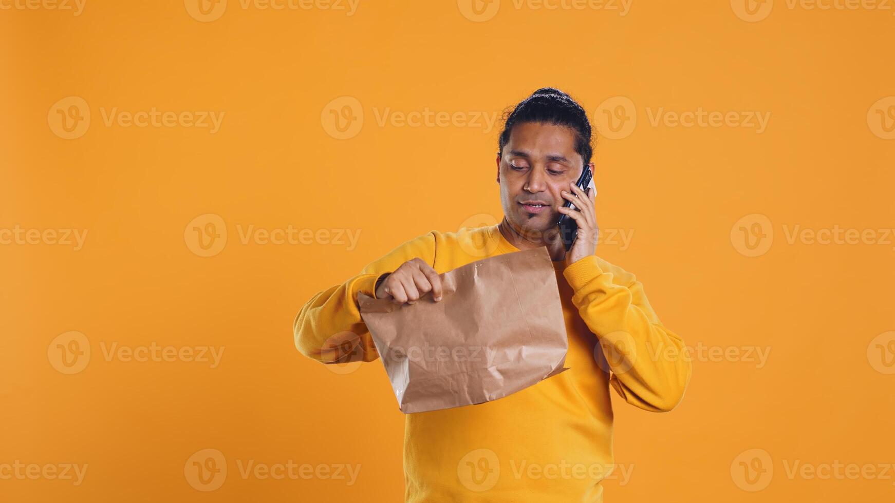 Delivery man arguing with customer on phone after arriving at destination and waiting for him, studio background. Indian person doing deliveries, scolding late client on telephone call, camera B photo