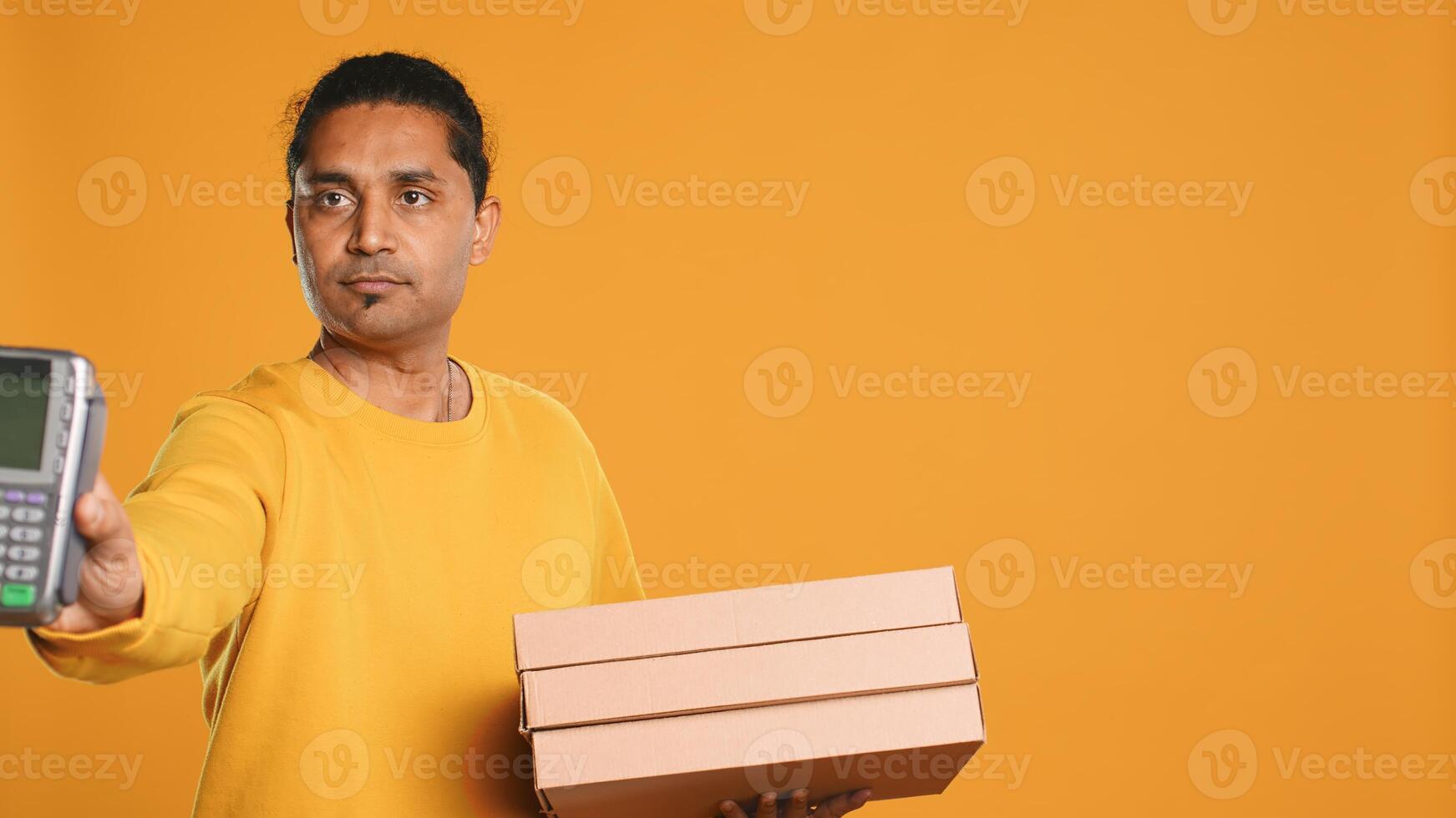 Portrait of indian pizza delivery man taking takeaway orders out of thermal backpack. Upbeat courier removing lunch boxes from transportation bag, isolated over studio background, camera A photo
