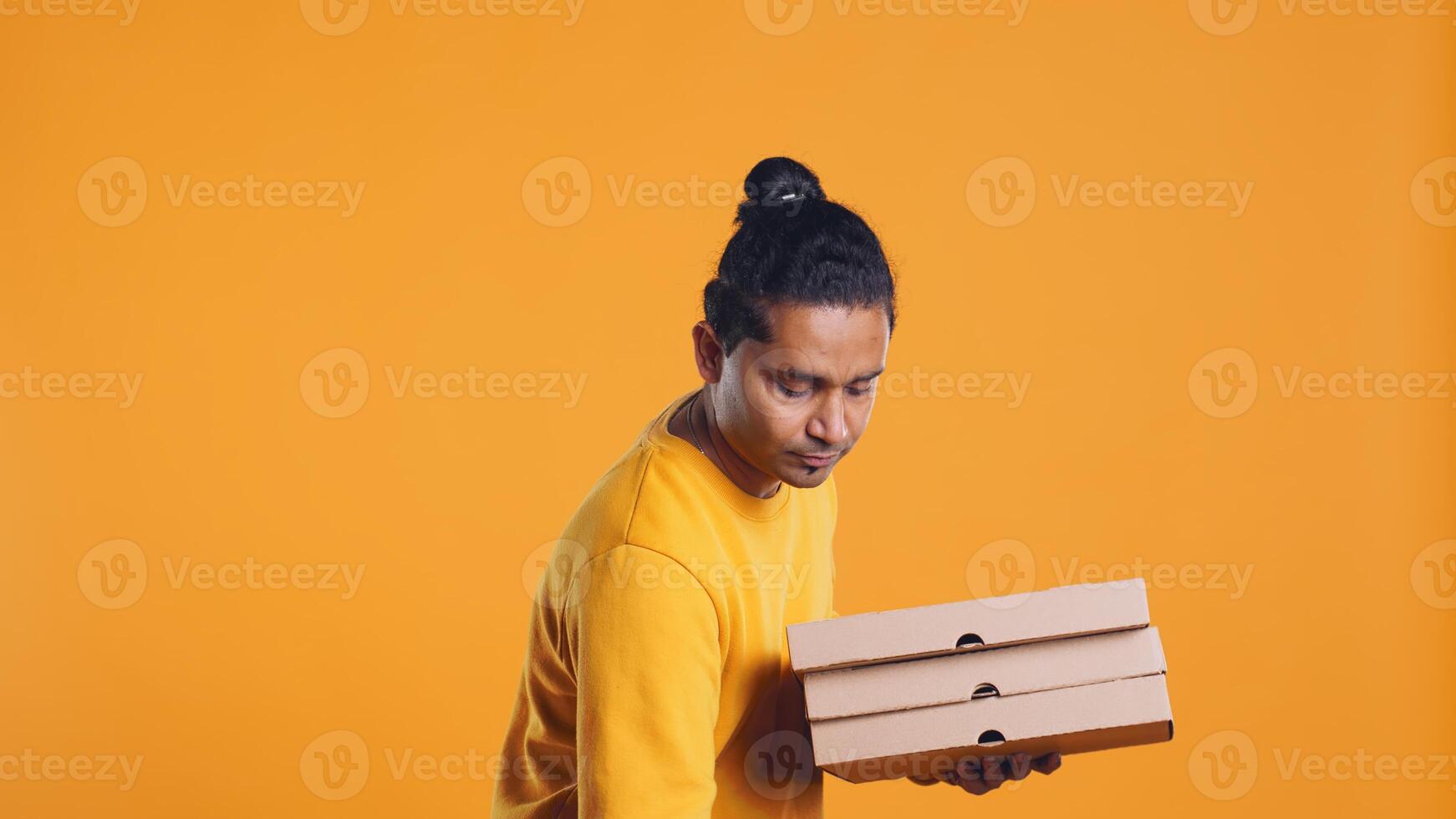 Portrait of indian pizza delivery man holding takeaway orders for customer. Upbeat courier with lunch boxes in arms and thermal food backpack, isolated over studio background, camera B photo
