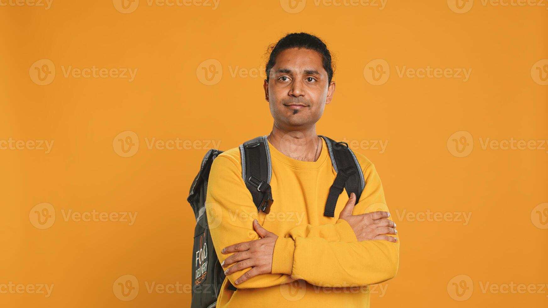 Portrait of happy smiling indian bike rider holding thermal backpack, isolated over studio background. Friendly courier prepared to deliver takeaway food to customer, camera A photo