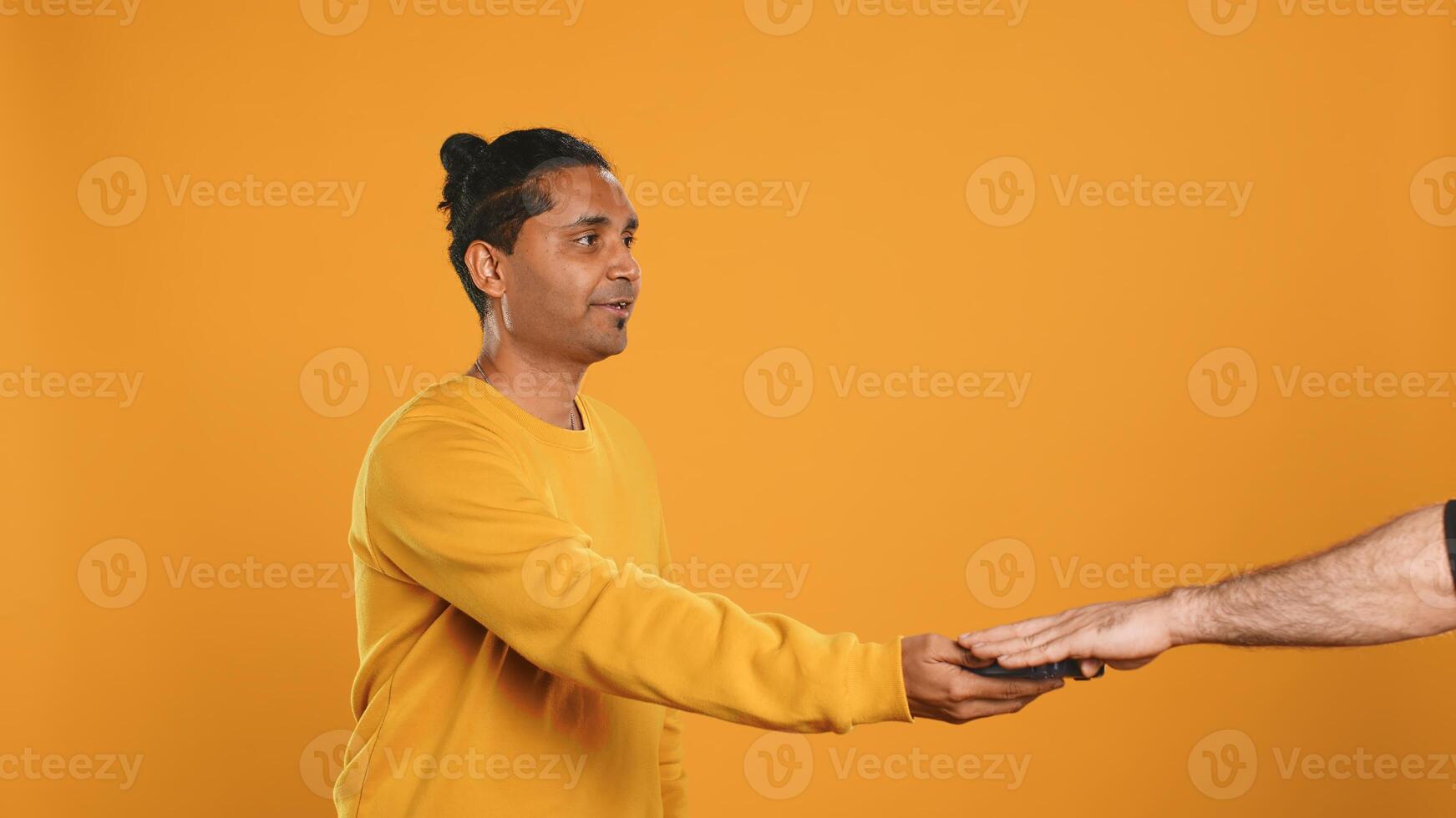 Indian pizza delivery worker getting takeaway order out of thermal backpack, giving it to client paying with card. Courier offering lunch paper bag and POS to customer, studio background, camera A photo
