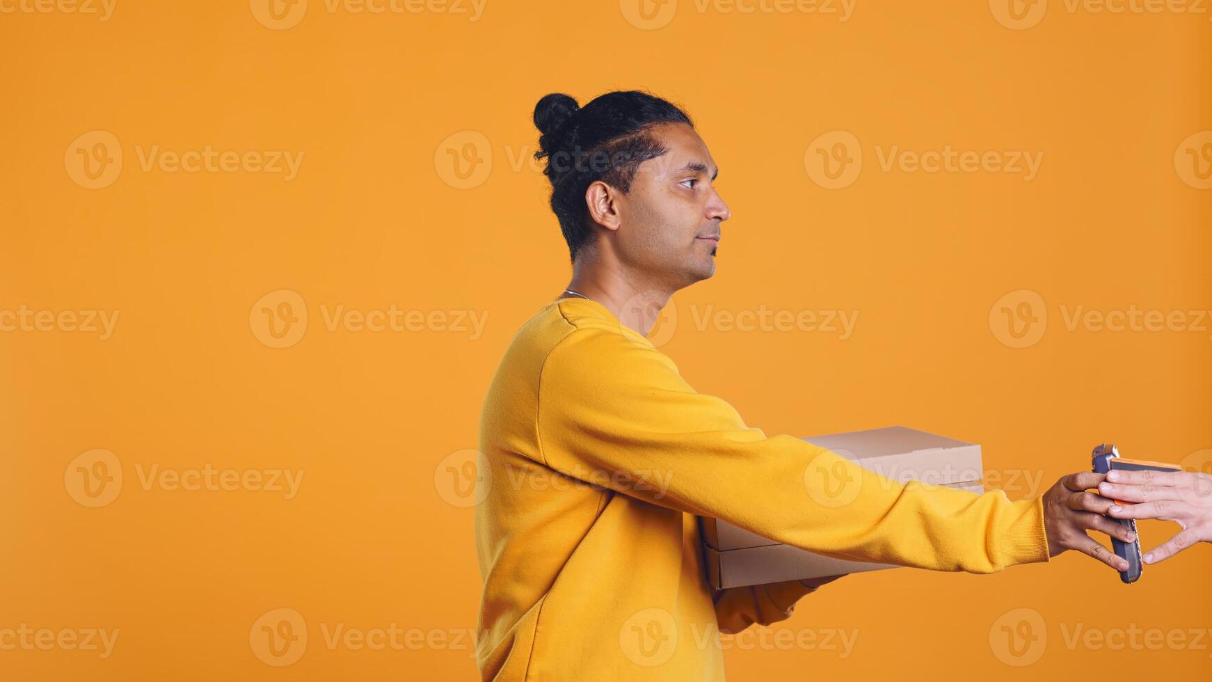 Pizza delivery man offering takeaway order to customer paying with credit card. Courier taking lunch boxes out of food backpack, giving POS to client to make transaction, studio background, camera B photo