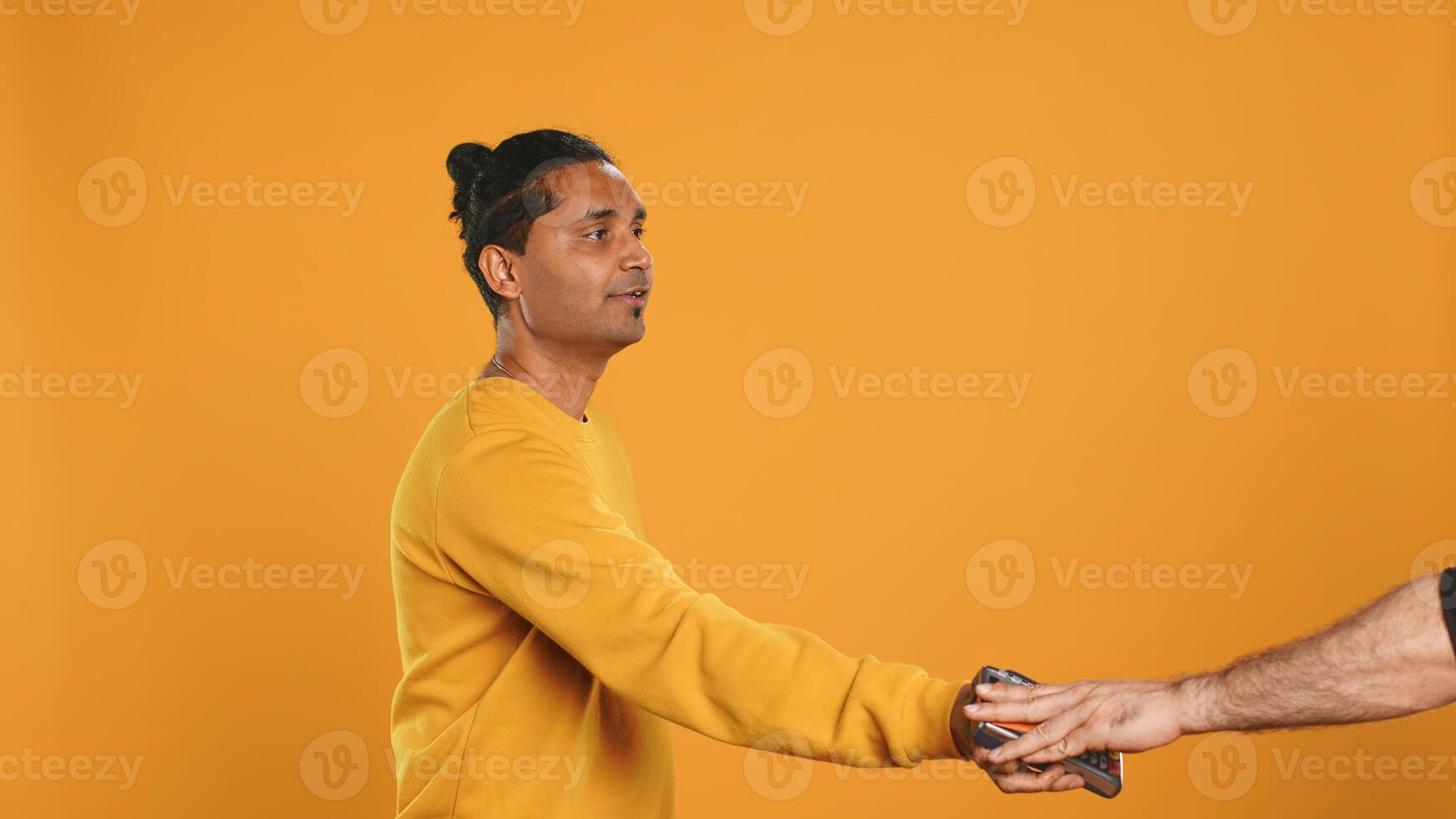 Friendly upbeat pizza delivery employee giving takeaway order to client paying with credit card. Asian man offering food order and digital payment method to customer, studio background, camera A photo