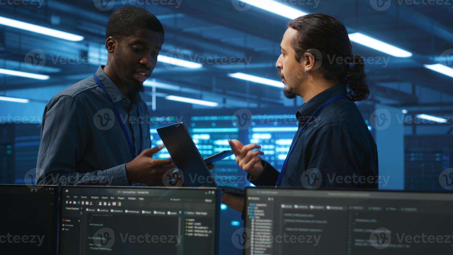 Engineers working in high tech server farm, using laptop and tablet to analyze data, ensuring seamless data flow. Men examining hardware in data center, ensuring system integrity and security photo