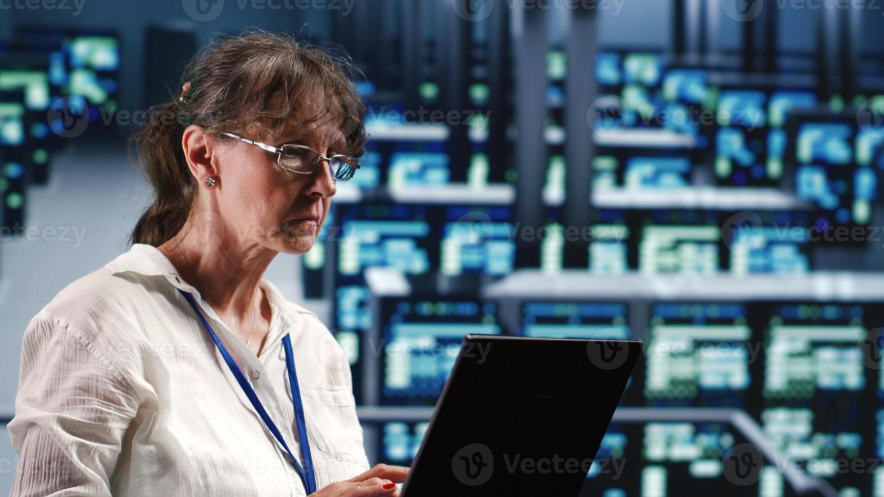 Elderly engineer in data center equipped to handle modern computing requirements, doing regular upgrades to components, increasing processing power, storage capacity and general efficiency photo