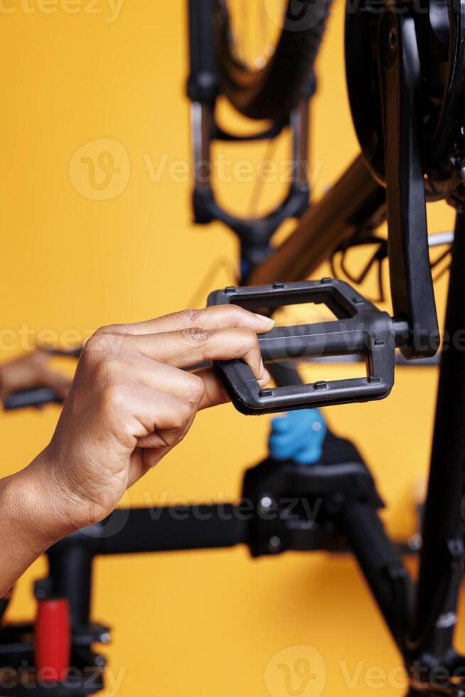 Photo focus on bicycle pedal being thoroughly inspected and maintained. Close up image of african american hand adjusting and servicing bike foot lever for leisure cycling.