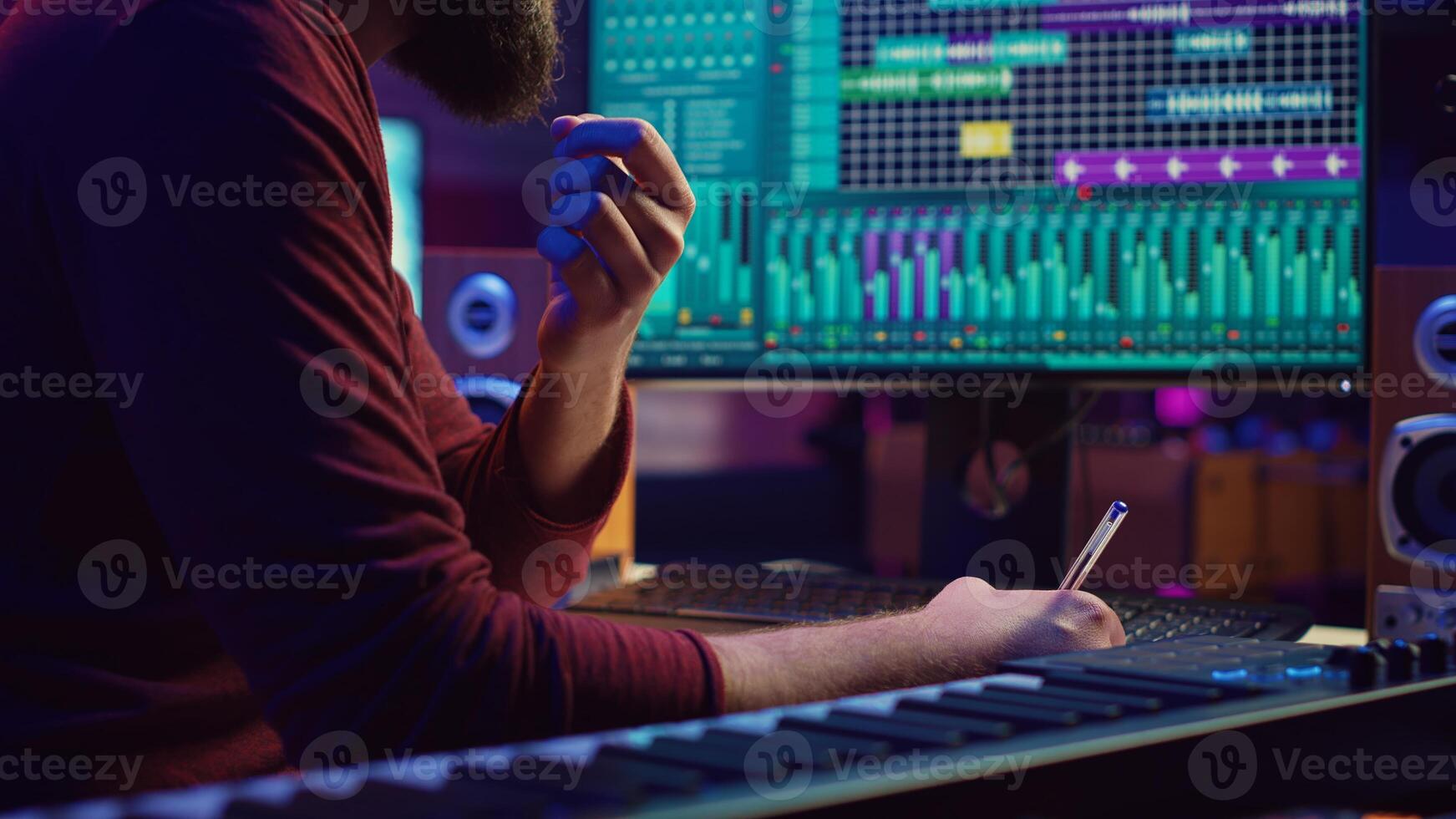 Songwriter creating a special song before recording tunes on musical instruments, writing down the words and melodic elements at his home studio. Artist producing sounds with DAW software. Camera A. photo
