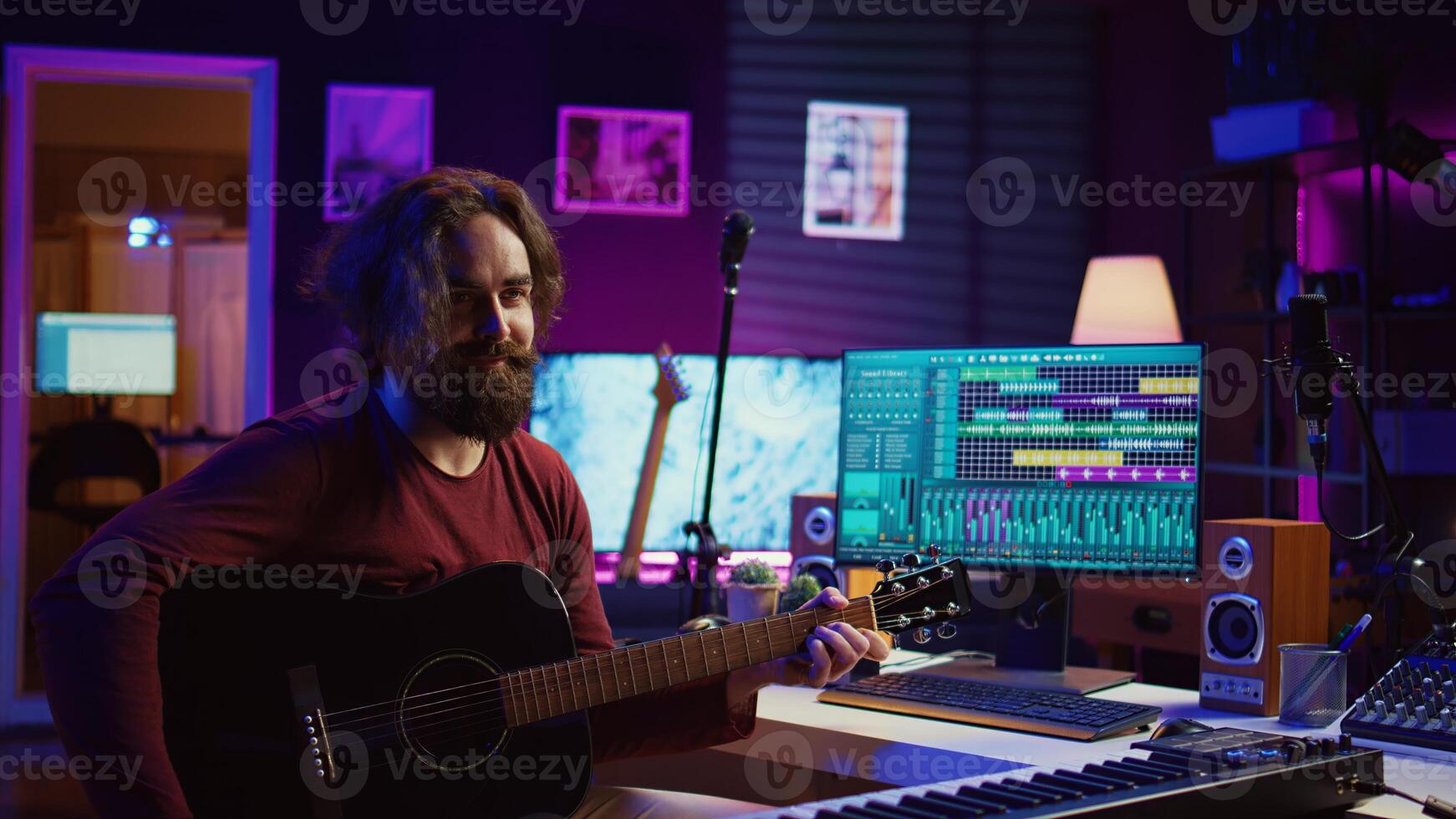 Young man songwriter playing guitar and creating music using equalizer program. Musician recording song in home studio, engineer mixing and mastering pop rock tracks. Camera B. photo