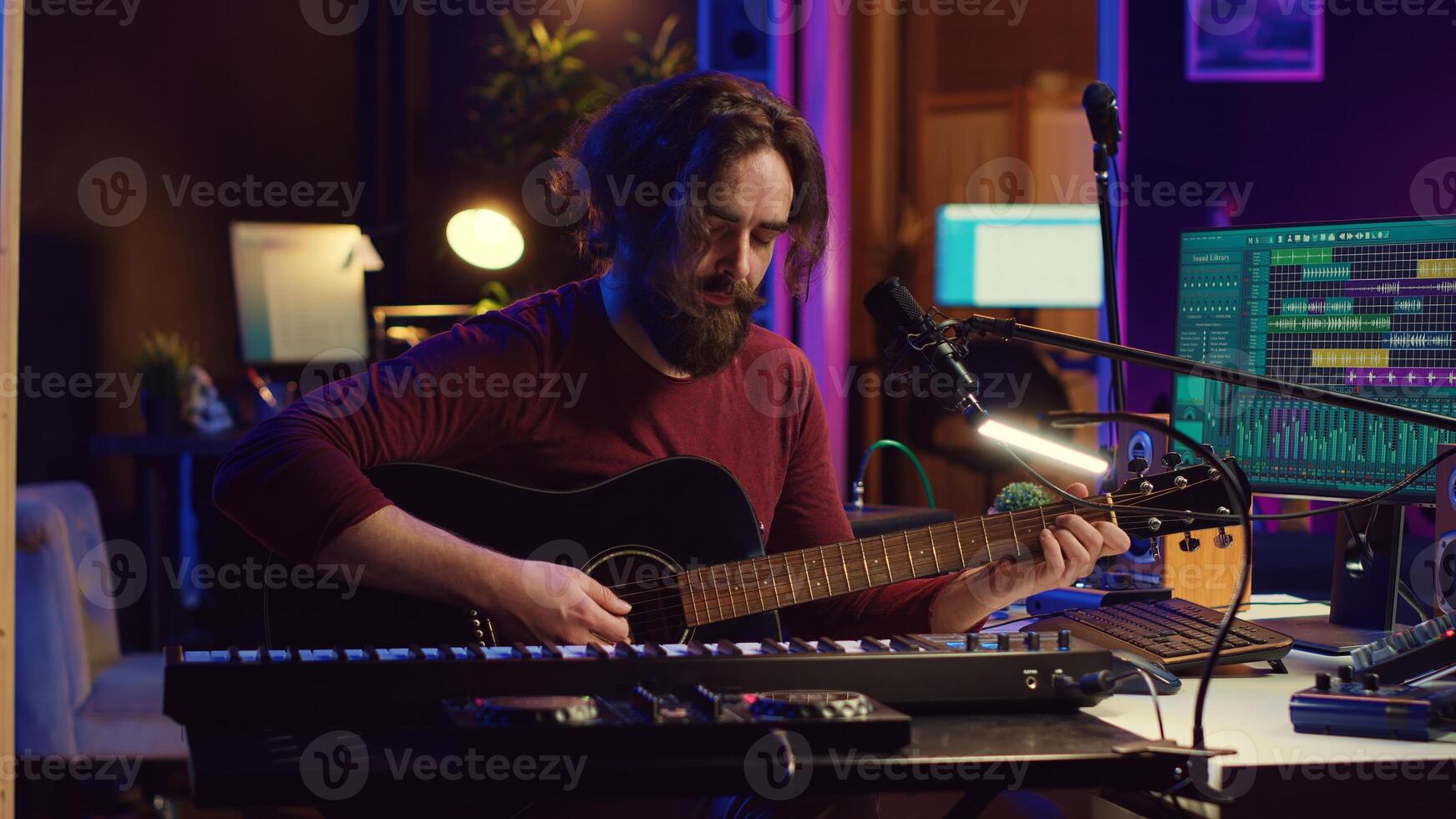 Music producer singing song and playing acoustic guitar, working in his personal home studio to record a new melody. Audio engineer recording tunes, editing with mixing console soundboard. Camera A. photo