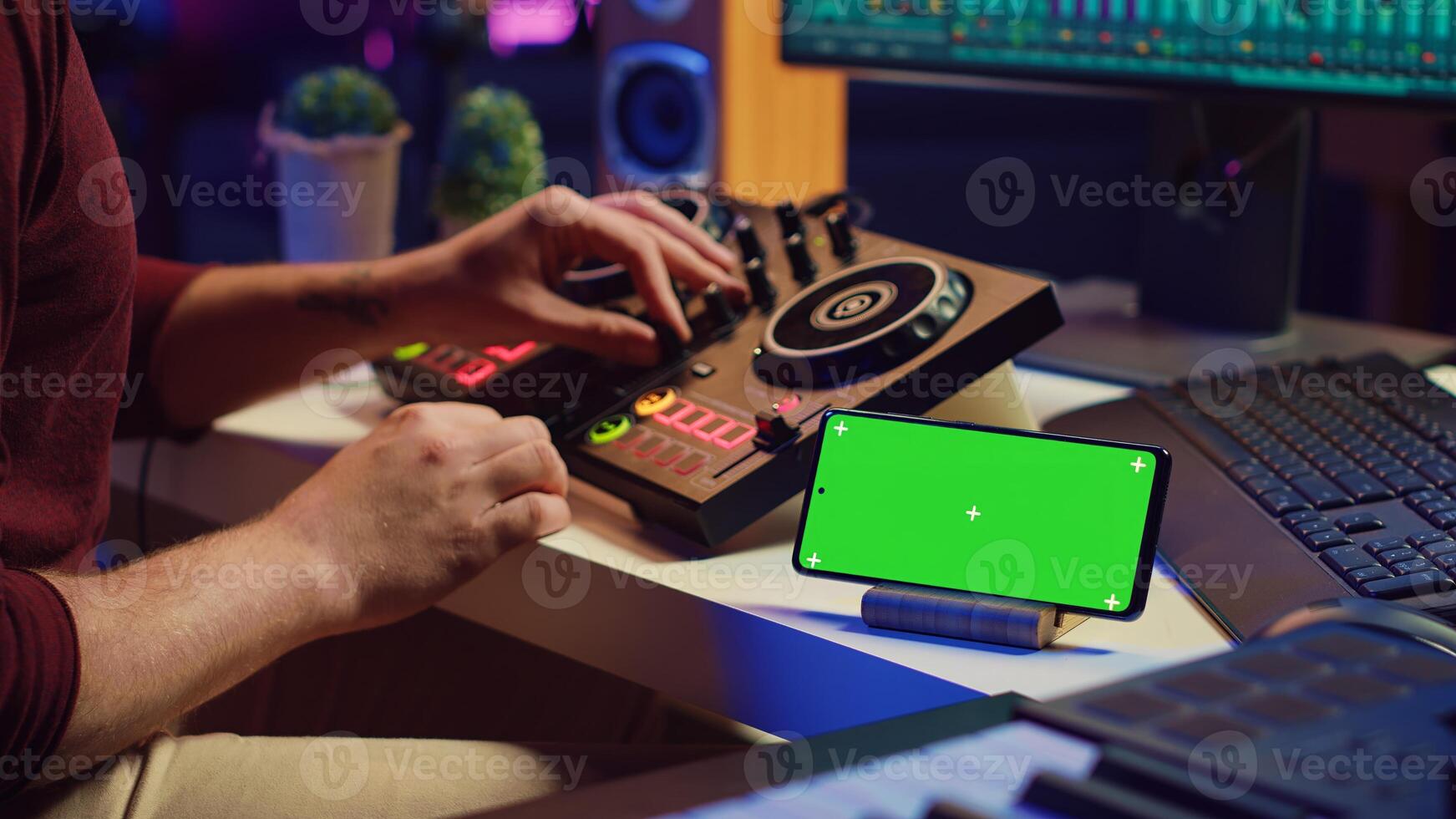 Musical performer creating mixed sounds and tunes with mixing console, greenscreen running on phone display. Artist recording new notes using equalizer and daw software on computer. Camera A. photo