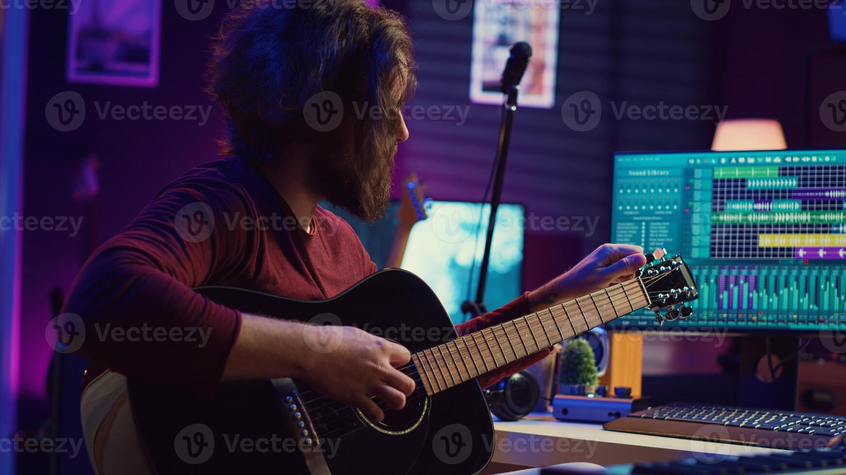 Music producer tuning his acoustic guitar before playing instrument, recording and mixing tunes to create new soundtracks. Singer composing a song using electronic panel controls. Camera B. photo