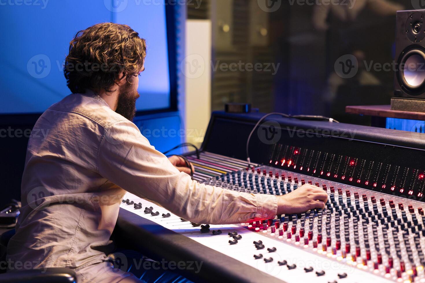 Tracking engineer applying mix and master techniques in studio, pressing buttons and sliders to add sound effects in post production. Skilled producer creating new music with audio console. photo