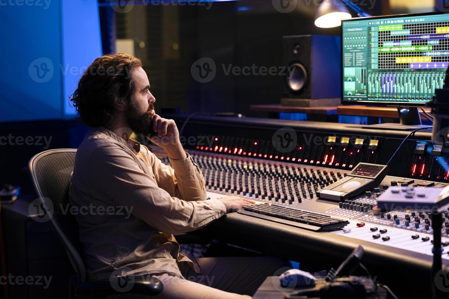 Tracking engineer uses audio console in professional recording studio, adjusting volume levels while pressing buttons on panel board. Skilled audio technician operates mixing and mastering gear. photo