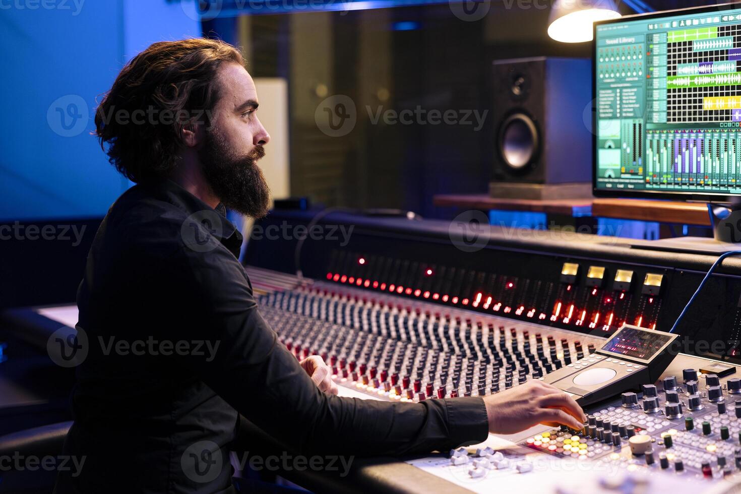 Tracking engineer editing new music with digital audio software and mixing console in control room, working in post production at studio. Audio technician operates sliders and knobs. photo