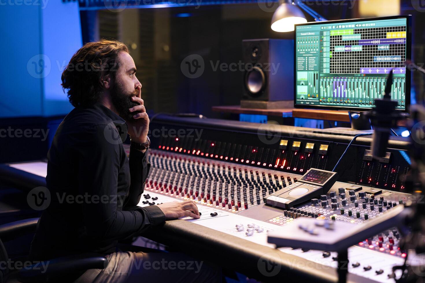 Tracking producer editing new records with digital software on pc and audio console in control room, working in post production at studio. Audio engineer operates faders and buttons. photo