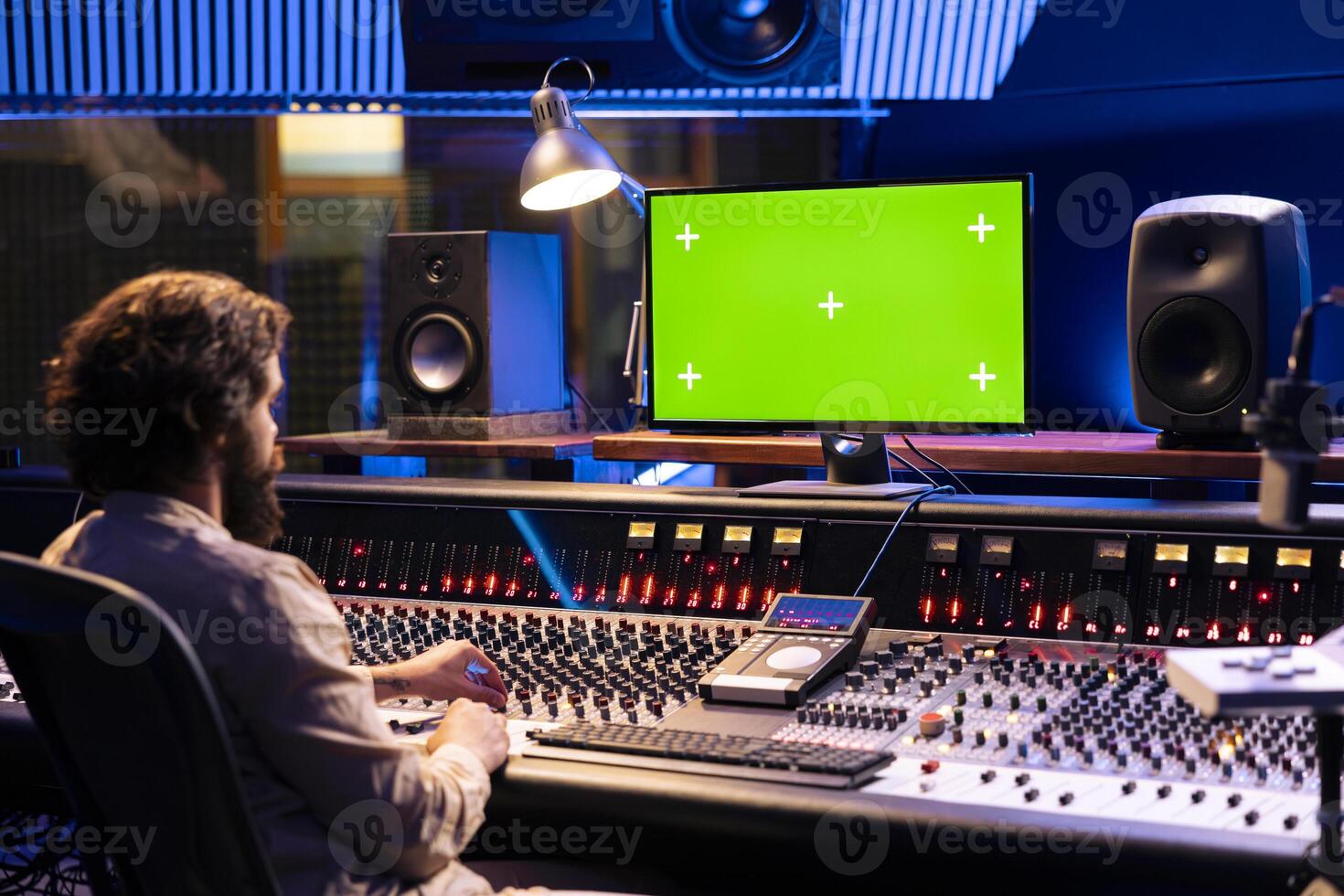 Audio engineer working in studio control room with greenscreen mockup, twisting knobs and switchers to produce music. Producer composer editing tracks and adding sound effects. photo