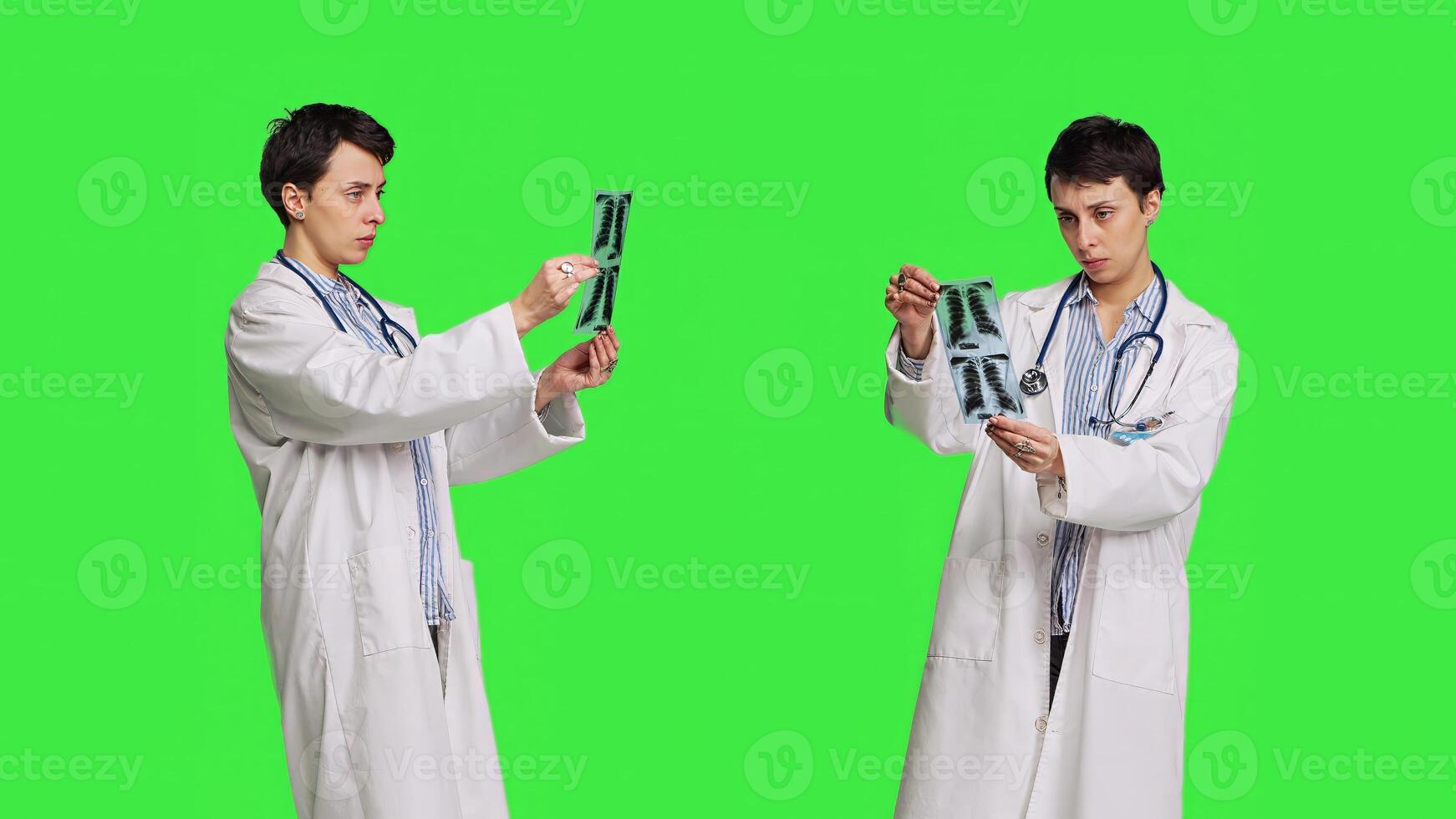 Woman doctor examines x ray scan to find disease diagnosis for patient, looking at radiography results to determine illness and cure. Medic standing against greenscreen backdrop. Camera B. photo