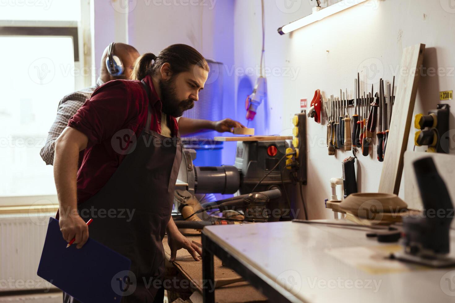 Quality assurance inspector holding notepad, inspecting workplace used to make wooden objects. Man doing control in furniture assembling workshop, making sure it meets safety measures photo