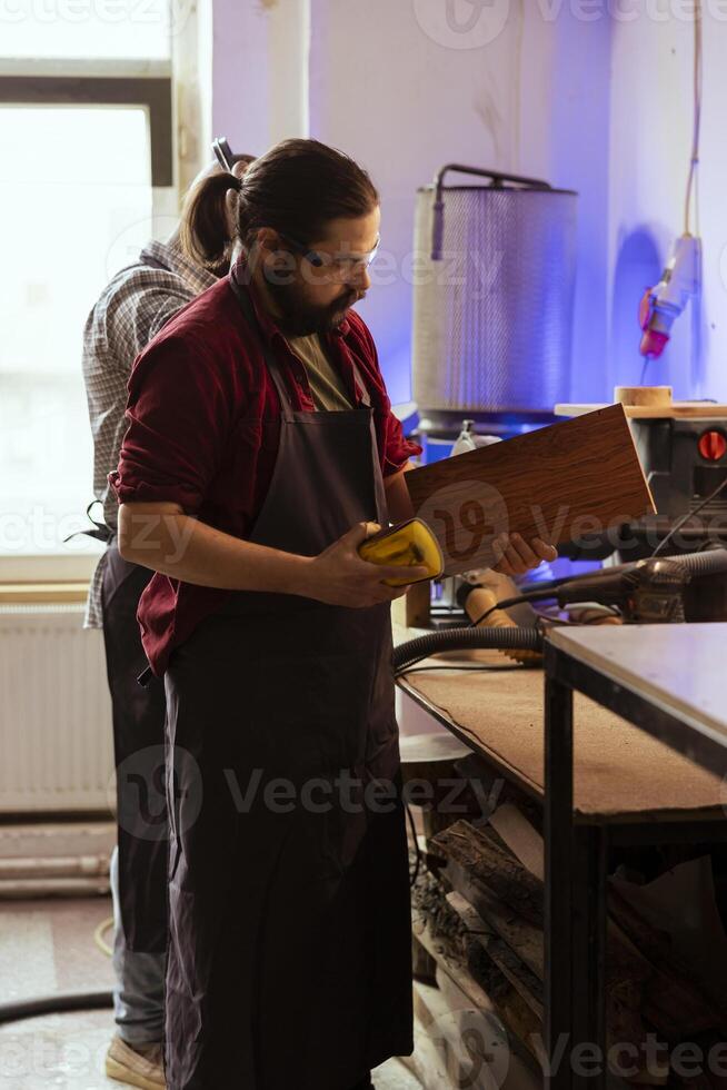 Artisan next to BIPOC coworker using sanding block to remove imperfections on wood piece. Creative person enjoying diy hobby, using sandpaper to do manual sanding near african american colleague photo