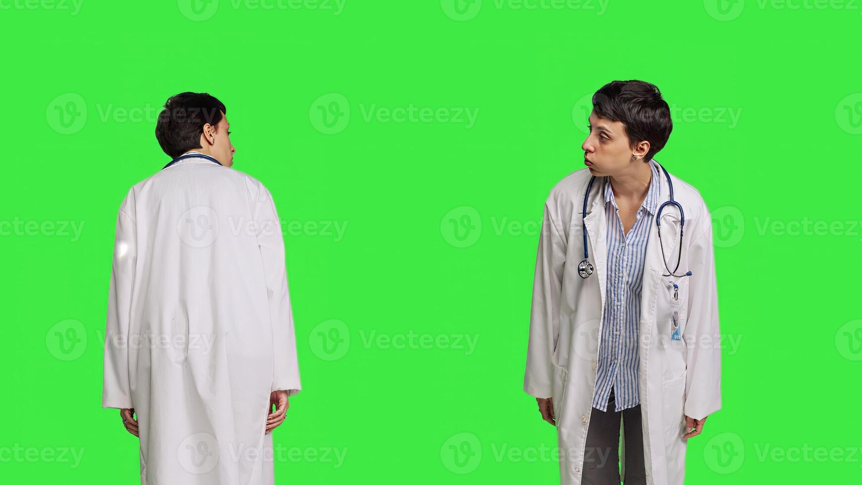 General practitioner feeling impatient waiting for patients at clinic, standing against greenscreen backdrop. Young physician with white coat looking around for people, medical exam. Camera B. photo