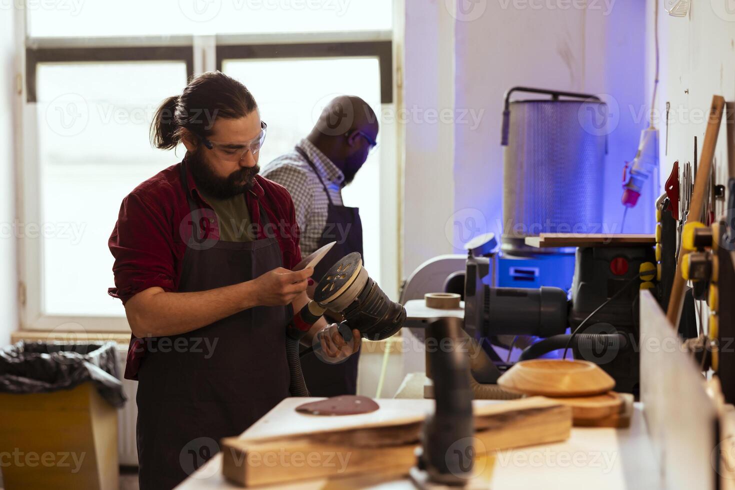 Carpenter holding power tool used to smooth surfaces by abrasion with sandpaper, changing cut off discs. Man preparing necessary equipment for furniture assembling job in studio photo