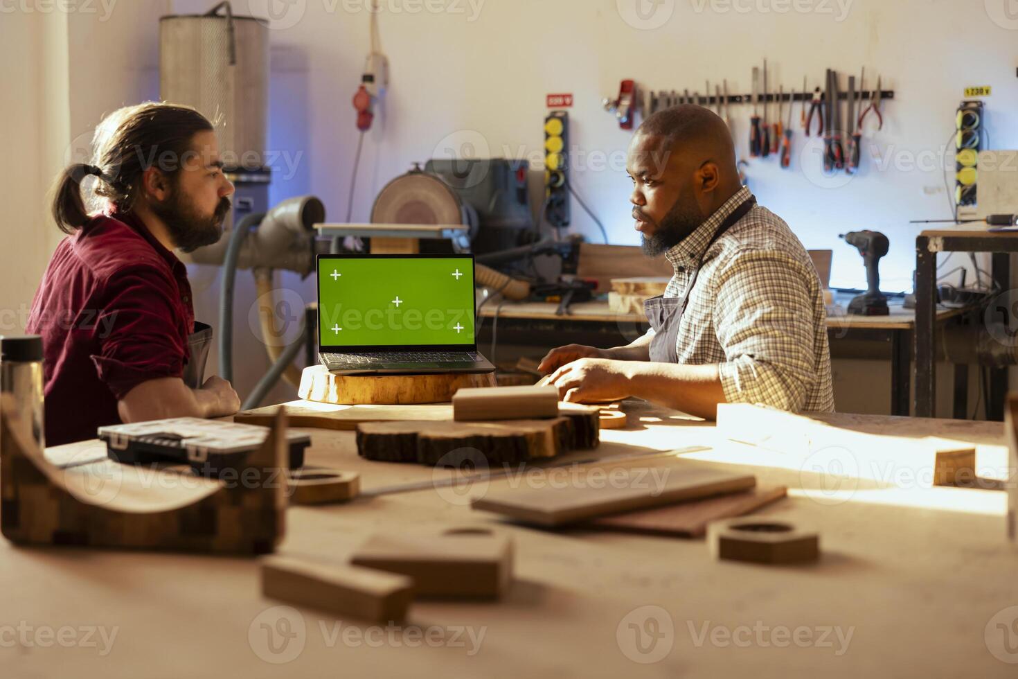 Cabinetmaker looking over blueprints schematics on isolated screen laptop in CAD software with apprentice. Woodworker and colleague designing custom 3D furniture on mockup notebook in assembly shop photo