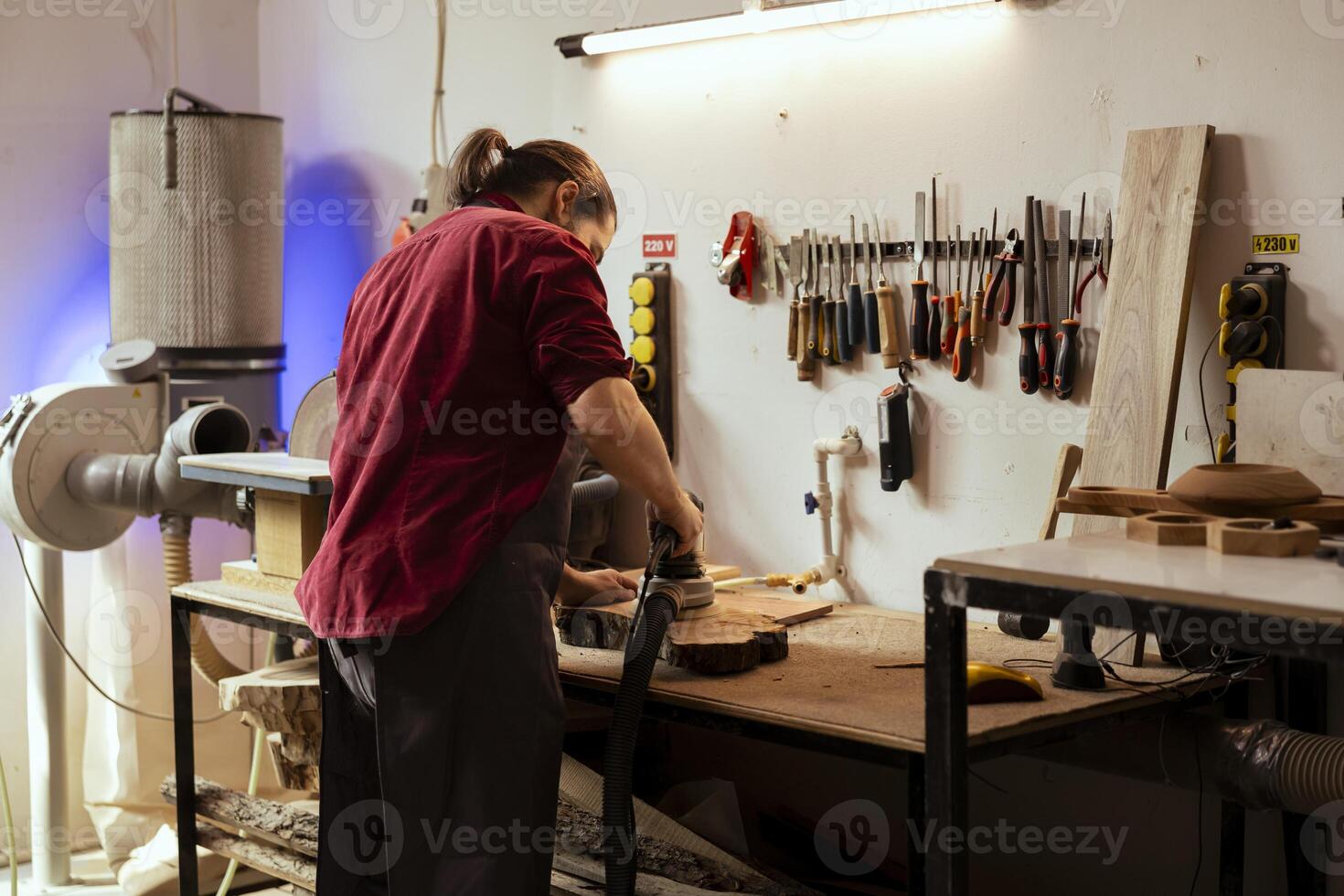 Artisan in studio using orbital sander with fine sandpaper on lumber to achieve smooth finish. Creative woodworker in carpentry shop uses angle grinder to create wood art photo