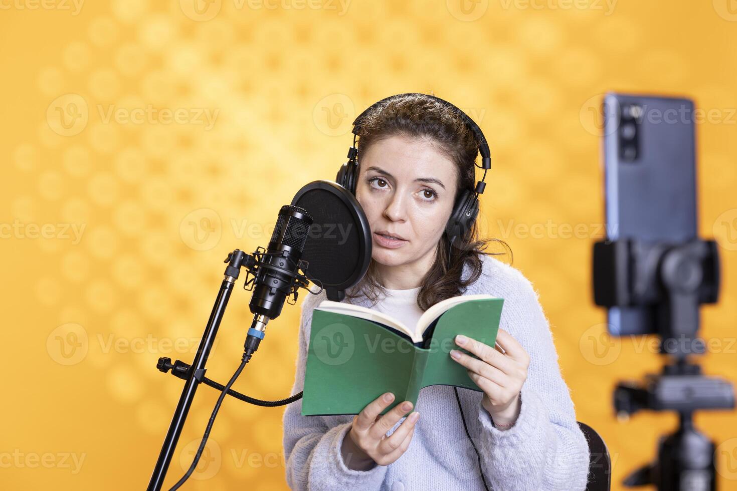 Media star filming vlog at work, reading book to record audiobook, isolated over studio background. Voice actor doing content creation while producing digital recording on novel using microphone photo