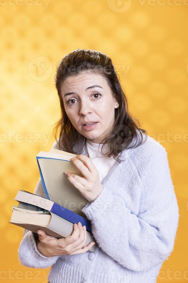Portrait of woman searching through stack of books in frenzy to gather information for school exam, studio background. Student nervous before university assessment, rushing to find necessary textbook photo